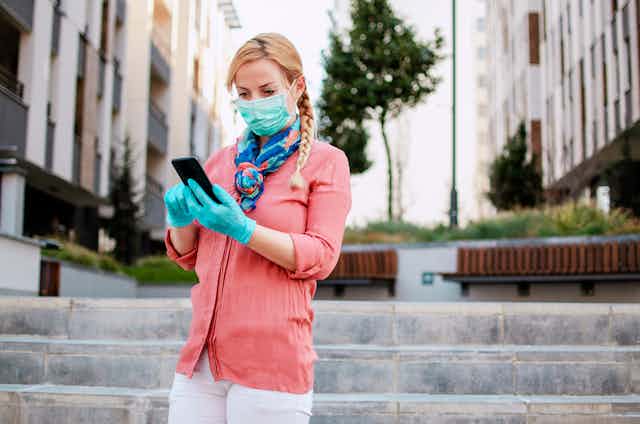 Woman wearing face mask and gloves looking at phone