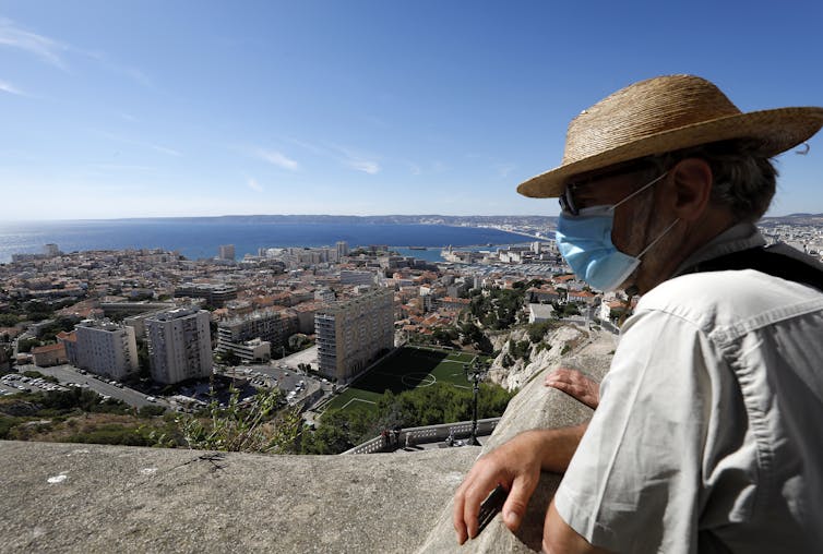 A man wearing a protective face mask looks out on Marseille.