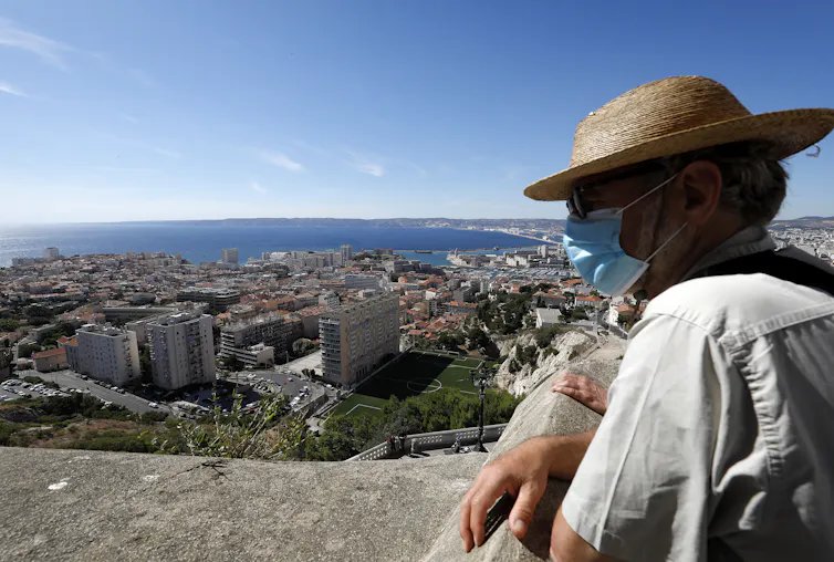 Un hombre con mascarilla y sombrero observa Marsella desde lo alto.