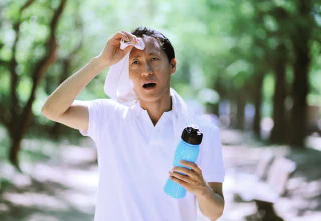 A man wearing a t-shirt holding a water bottle and wiping sweat off of his brow.