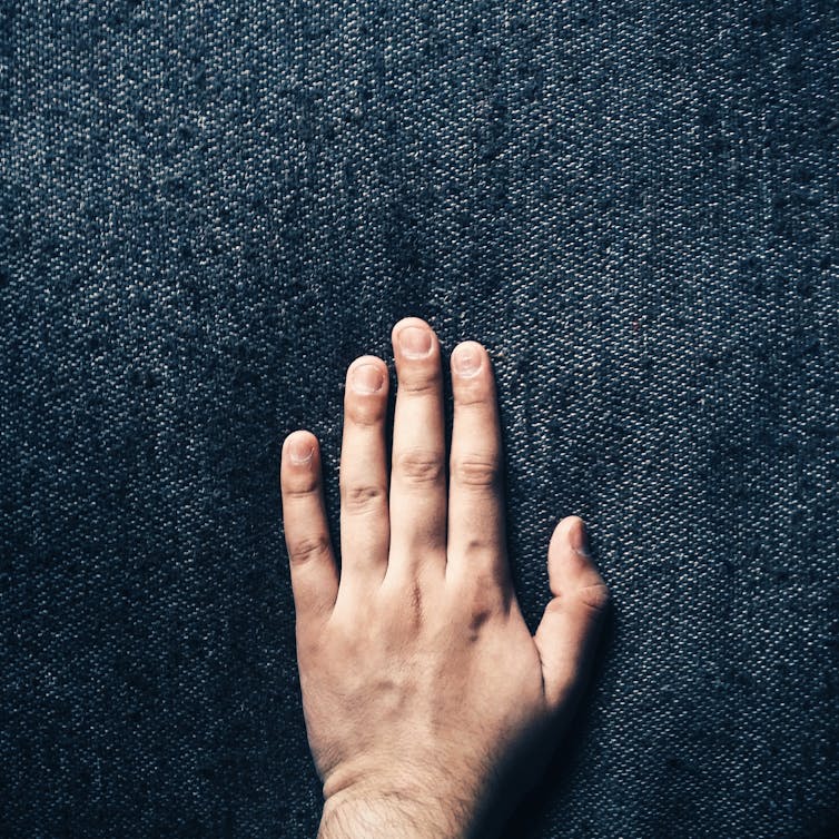 A hand touching a dark blue fabric.