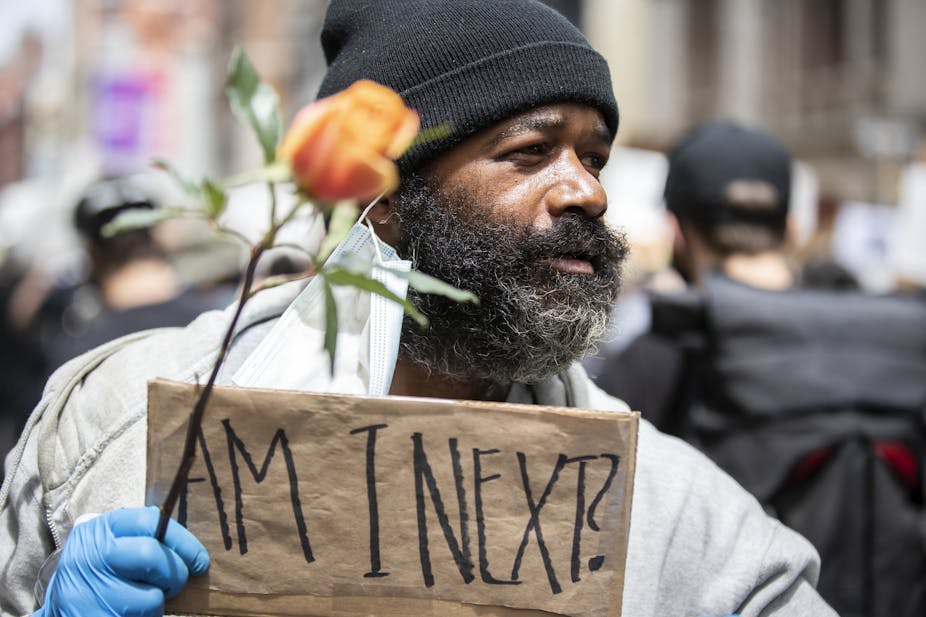 A Black man at a demonstration holding a sign, "Am I next?"