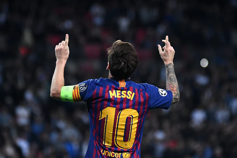 Lionel Messi de espaldas, con camiseta del Barça, señalando al cielo con los índices de las manos.