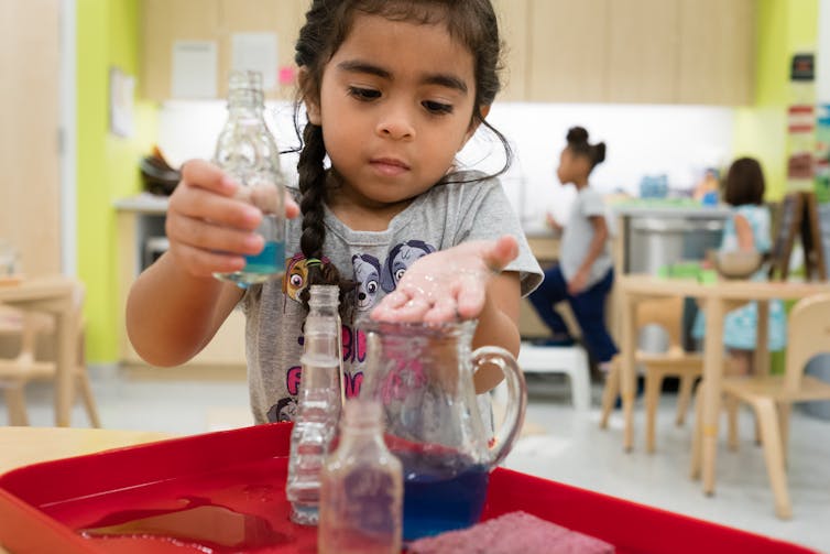 A toddler fills bottles with water.