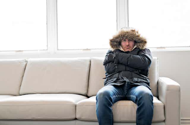 Man in thick jacket sitting on couch in cold house