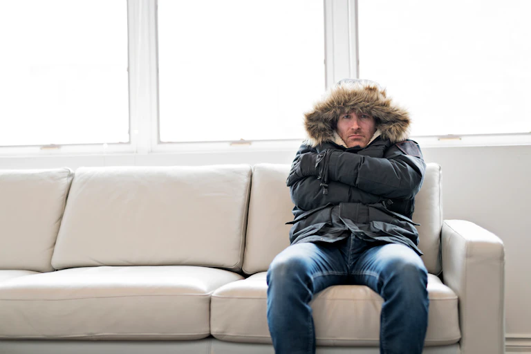 Man in thick jacket sitting on couch in cold house