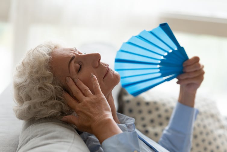 Elderly women fanning herself as she struggles with the heat in her house