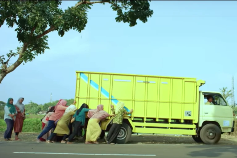Women pushing a truck on the side of the road in in the film _Tilik_.