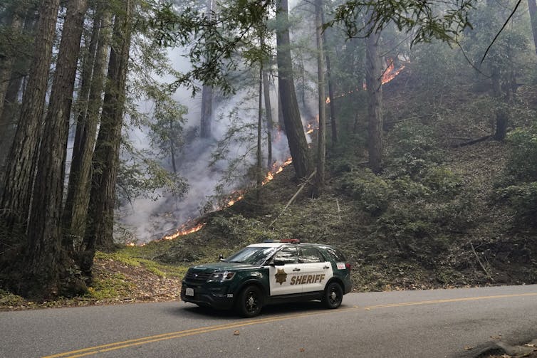 Police car in California drives through burning forest.