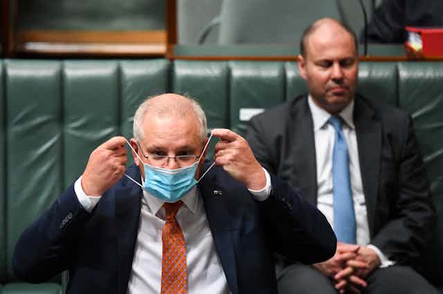 Scott Morrison puts on a mask, in the House of Representatives, with Josh Frydenberg in the background