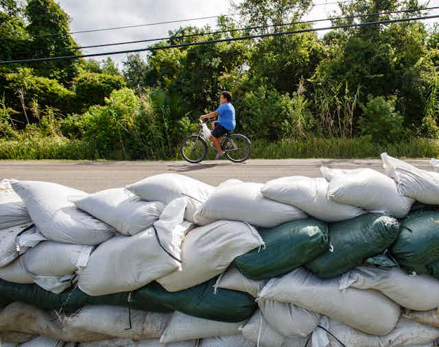 A child cycles past a wall of sand bags.