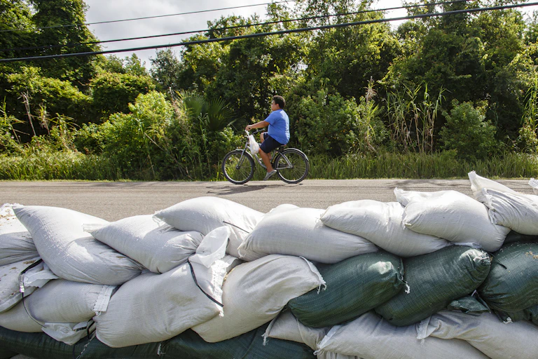 A child cycles past a wall of sand bags.