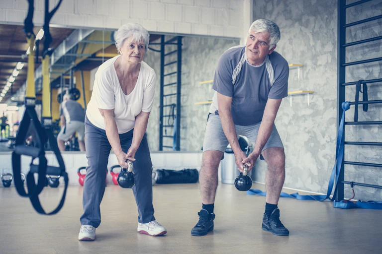 Older couple lifting kettlebells at the gym.