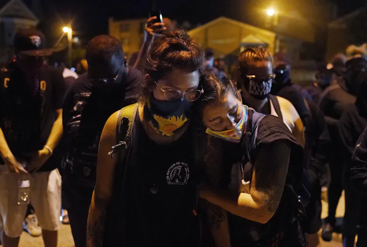 People wearing masks embrace by candlelight.