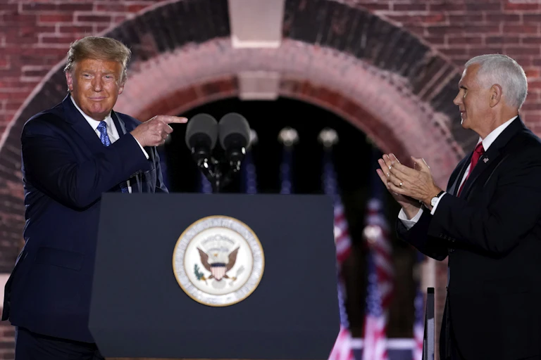 Donald Trump points across a podium at Mike Pence, who applauds him.