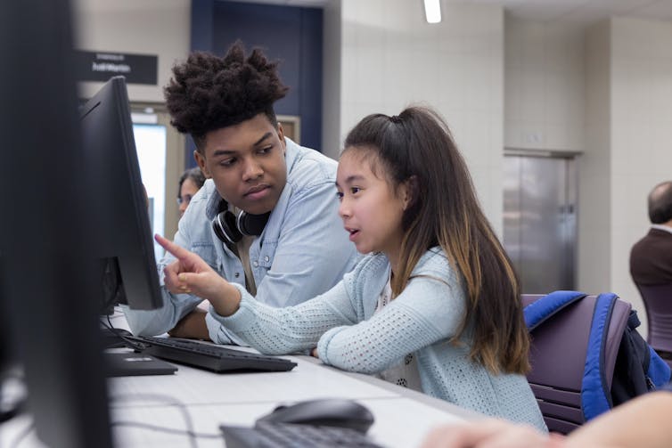 An Asian American girl points at a computer screen with African American female teacher.