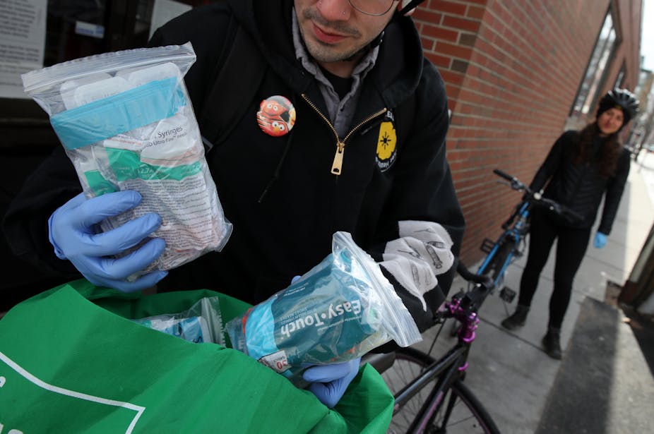 A man with gloves holding a bag of safe injection supplies.