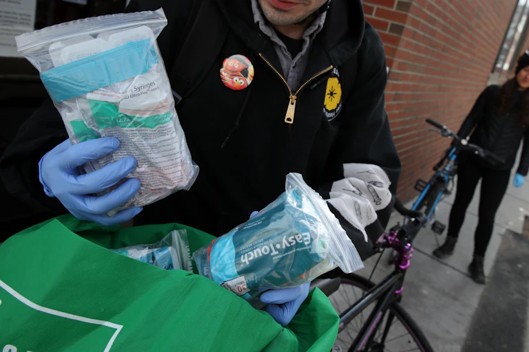 A man with gloves holding a bag of safe injection supplies.