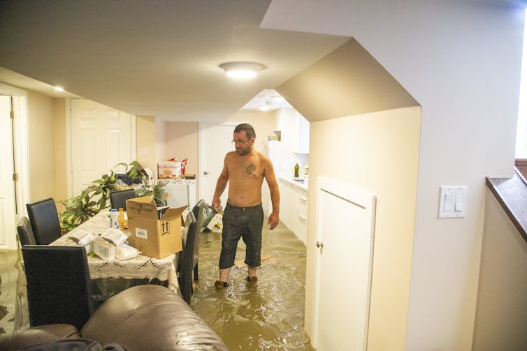A man stands in shin-deep water in an apartment.