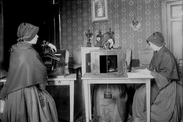 Hermanas de la orden de Maria Bambina utilizando microscopios para revisar placas fotográficas. A la derecha, una de las ellas anota coordenadas de estrellas. 
