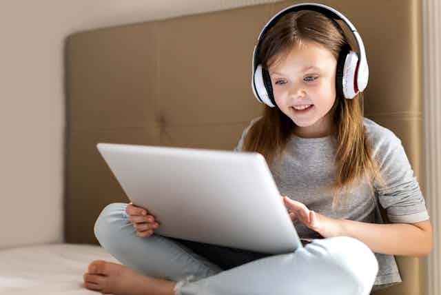 Young girl sitting on bed watching something on laptop.