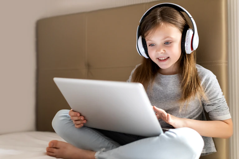 Young girl sitting on bed watching something on laptop.