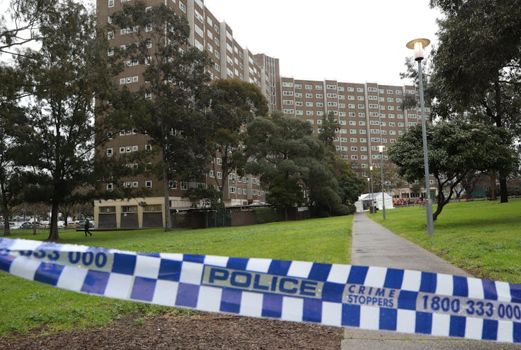 A police tape crosses in front of a path leading to housing towers.