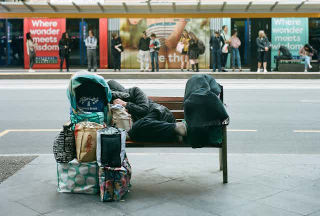 Homeless person resting on bench with belongings piled in front