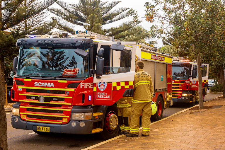 Firefighters getting into a fire truck beside a footpath.