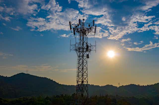 A 5G mobile tower silhouetted against hills and a low sun.