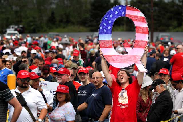A man holds up a large 'Q' sign while waiting in line to see President Donald Trump at a rally.