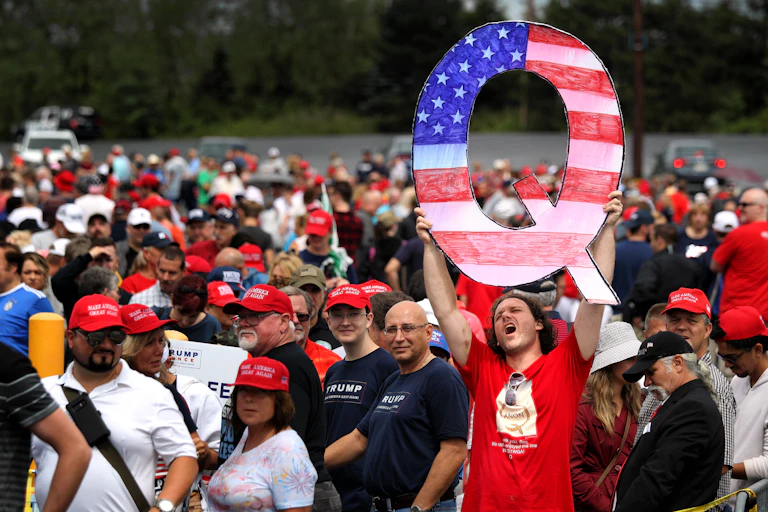 A man holds up a large 'Q' sign while waiting in line to see President Donald Trump at a rally.