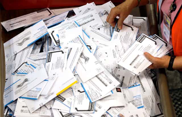A person picks up mailed-in ballots from a large box of them.
