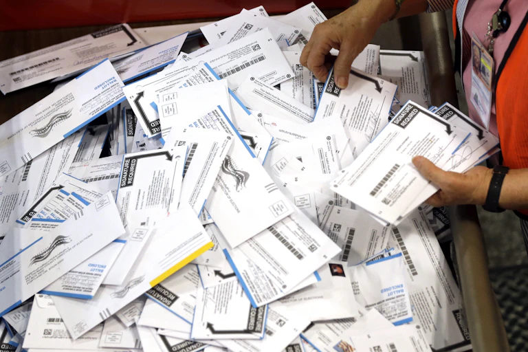A person picks up mailed-in ballots from a large box of them.