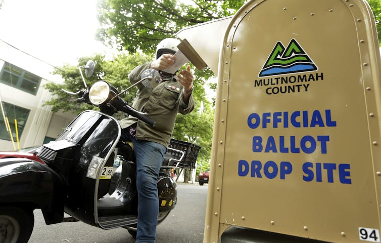 A motorcyclist puts a ballot in a drop box.