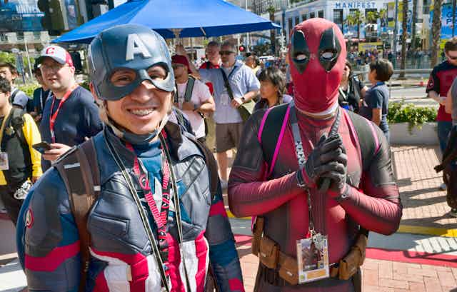 People dressed as Captain America and Deadpool stand in front of a crowd.