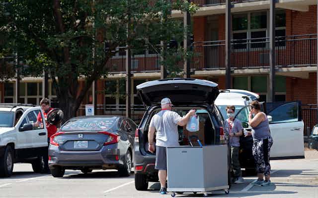 Parents help college students pack cars in a parking lot. 