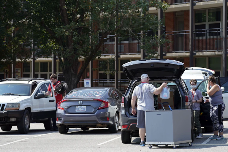 Parents help college students pack cars in a parking lot.