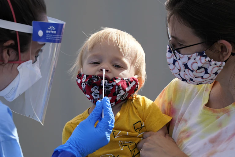 A medical professional inserting a swab into the nose of a child being held by his mother.