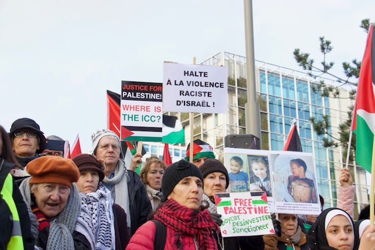 Protesters in front of the ICC building hold sigs saying 'Where is the ICC?' and 'Justice for Palestine'
