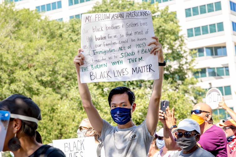 A young Asian man at a protest with a sign that says 'Black Lives Matter.'