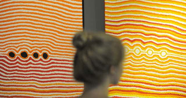A woman stands in front of two vibrant dot paintings