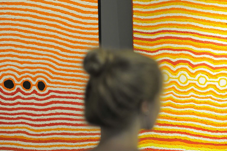 A woman stands in front of two vibrant dot paintings