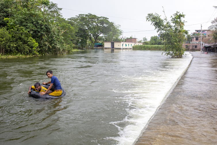 Two boys use a rubber tube to float in a flooded street in Bangladesh