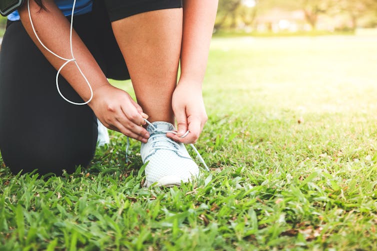 A woman crouched on the grass ties up her running shoe.