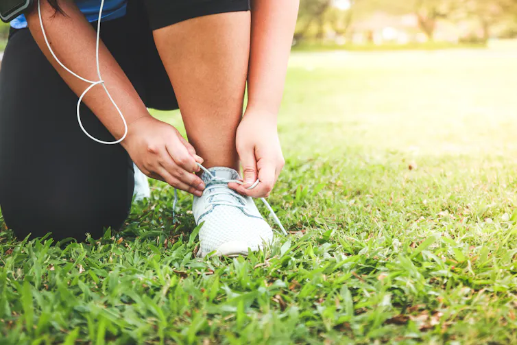 A woman crouched on the grass ties up her running shoe.