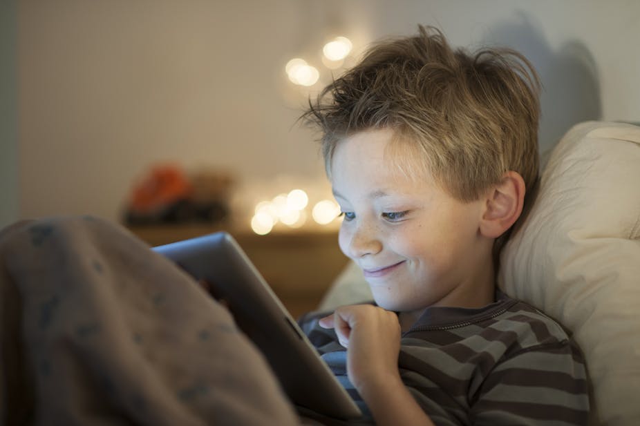 A young boy in bed and smiling while watching something on his iPad