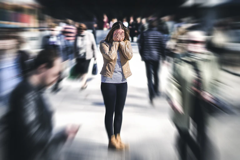 Woman in busy crowd with hands over her face.