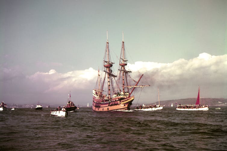 Replica of the Mayflower sailing surrounded by other smaller ships.