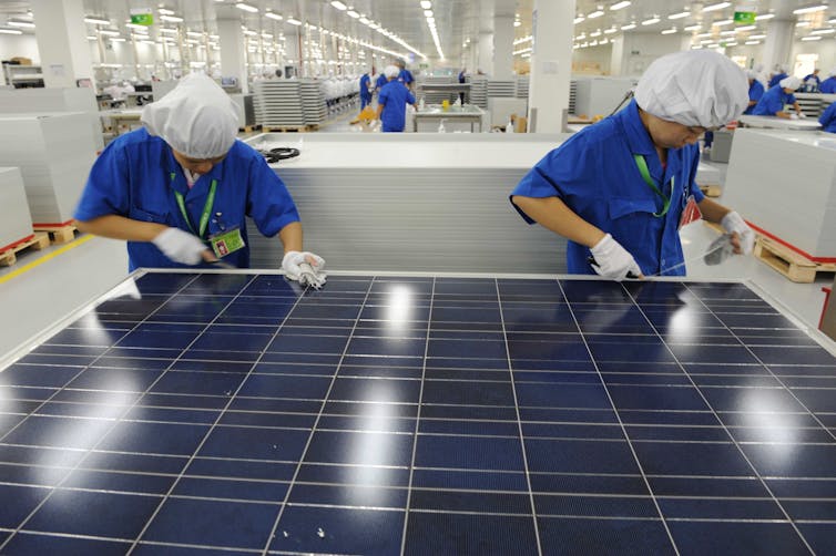 Two workers with white gloves work on a solar panel.
